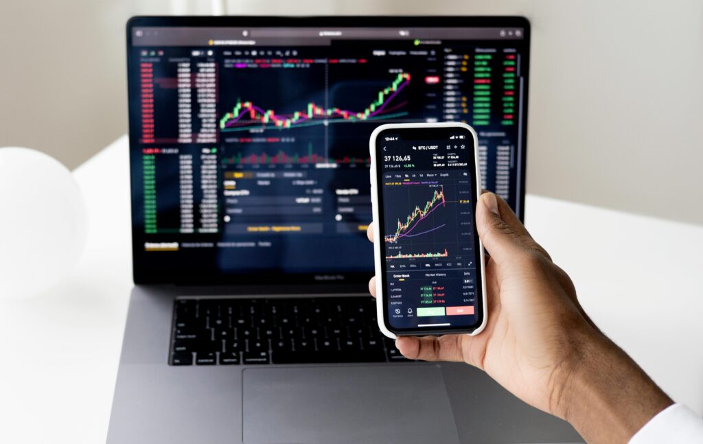 Pessoa analisando gráficos financeiros no celular e notebook, simbolizando a facilidade e mobilidade para investir em fundos imobiliários.