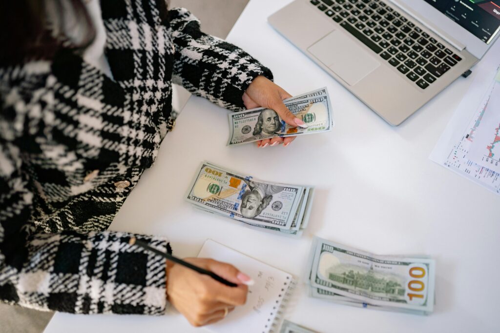 Mulher organizando dinheiro e fazendo anotações em bloco de notas, representando controle financeiro e planejamento de investimentos.