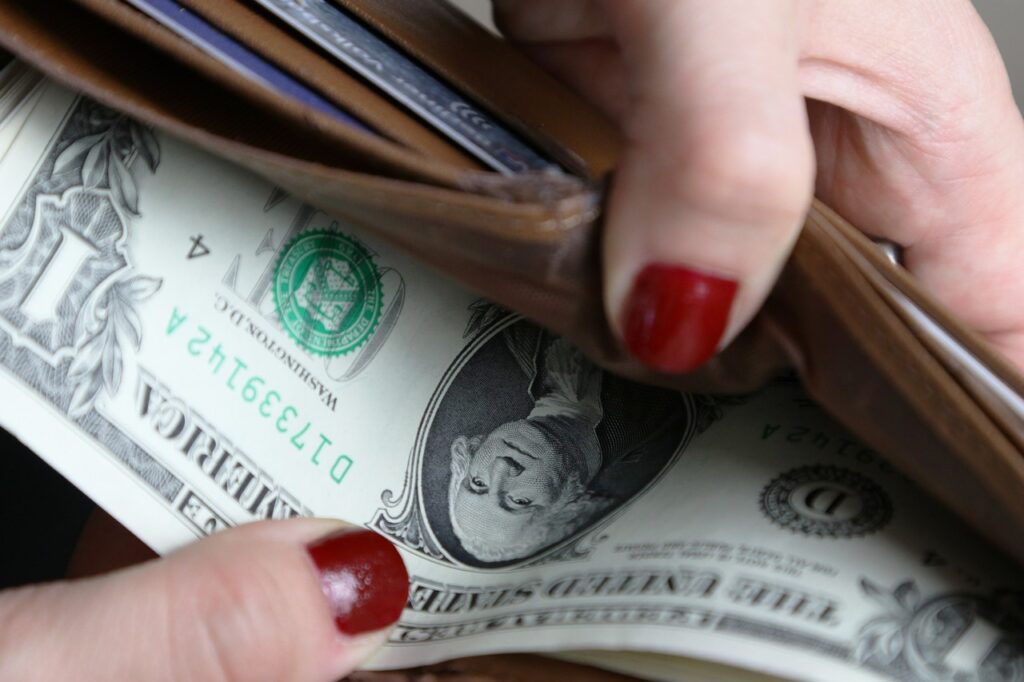 Mão segurando carteira com notas de dólar representando dividendos de ações brasileiras.